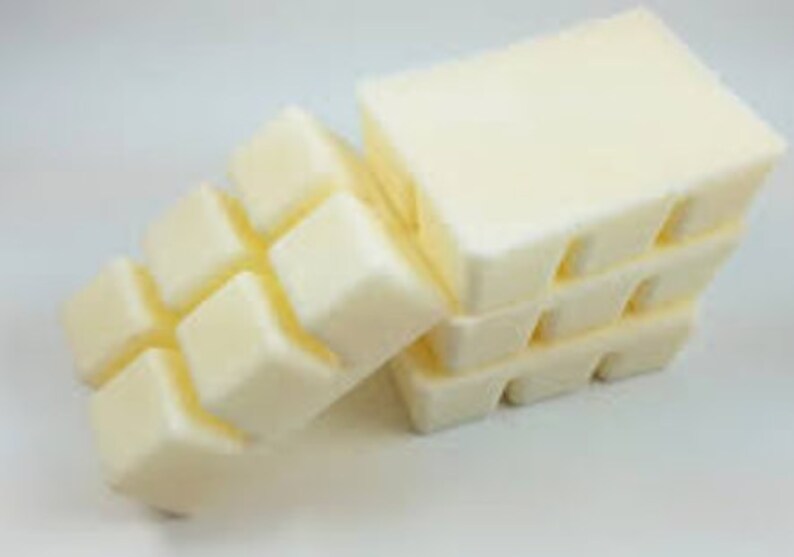 May include: Cream-colored wax melt cubes arranged in a stack and a row. The cubes are rectangular with rounded edges, suggesting a smooth texture. The wax melts are a light, off-white color.