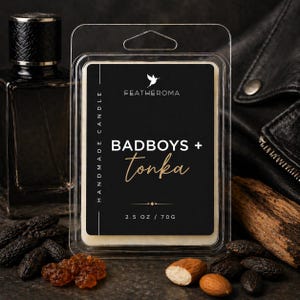 May include: A black and white label reads "FEATHEROMA" and "BADBOYS + tonka" on a handmade candle. The candle is in a clear plastic container. The label also states "2.5 OZ / 70G". The candle is surrounded by ingredients and a dark perfume bottle.