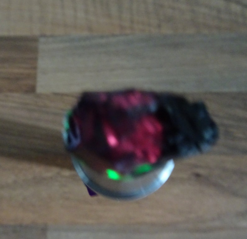 Puede incluir: Primer plano de un spinner de mano rojo y negro con una luz verde que brilla desde el centro.