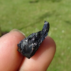 Puede incluir: Un cristal de obsidiana negro con una punta afilada y matices iridiscentes verdes y azules.