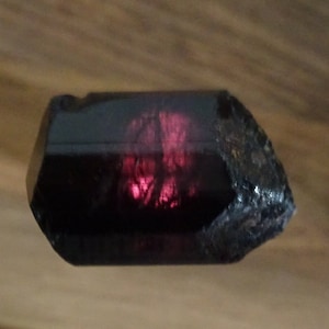 May include: A dark purple crystal with a red, translucent center. The crystal has a rough, natural texture.