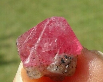 May include: A pink ruby crystal with a rough, natural appearance. The crystal has a sharp, faceted shape and is translucent.