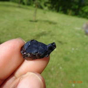 Puede incluir: Una roca de obsidiana oscura, negra y verde con una forma irregular y rugosa.
