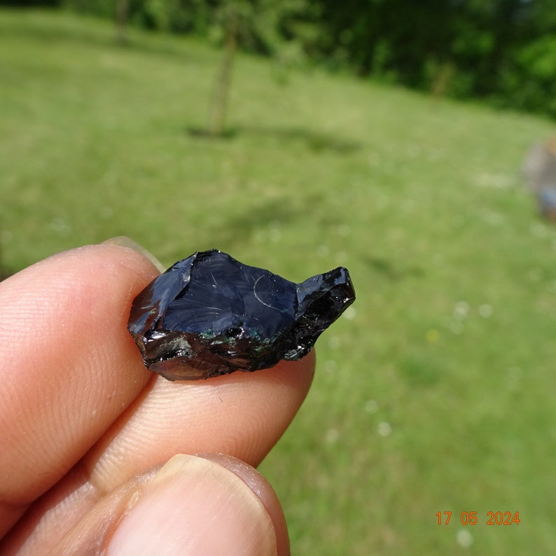 Puede incluir: Una roca de obsidiana oscura, negra y verde con una forma irregular y rugosa.