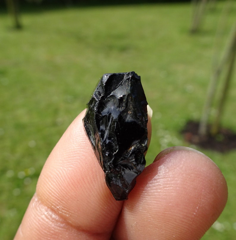 Puede incluir: Una punta de flecha de obsidiana negra con una punta afilada y una superficie rugosa y texturizada.