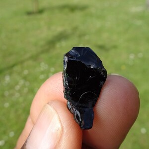 Puede incluir: Una roca de obsidiana negra con una forma irregular y rugosa. La roca tiene una superficie brillante y vidriosa.