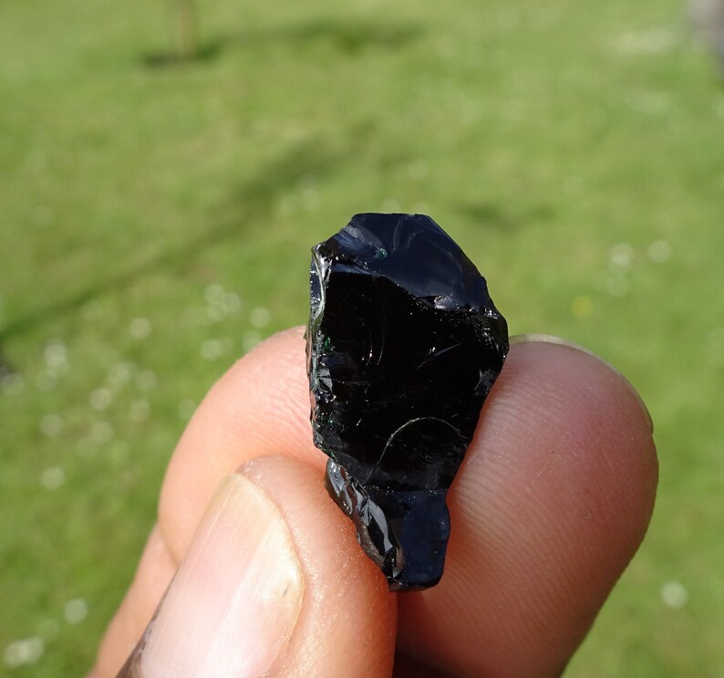 Puede incluir: Una roca de obsidiana negra con una forma irregular y rugosa. La roca tiene una superficie brillante y vidriosa.