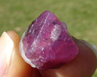 May include: A pink and purple gemstone with a rough, faceted surface. The gemstone is a natural crystal with a translucent appearance.