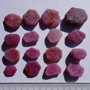 Puede incluir: Una colección de 15 piedras preciosas de rubí rosa en bruto. Las piedras son de varias formas y tamaños, algunas tienen una forma más hexagonal.