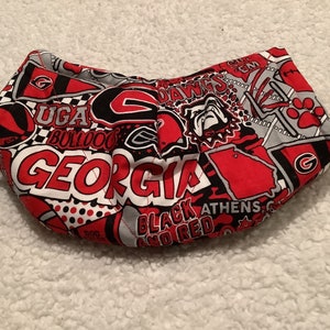 May include: Red and black fabric with a comic book style design featuring the words "UGA Bulldogs", "Georgia", "Dawgs", "Athens", and "Black and Red".