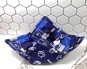 May include: A blue and white bowl cozy with a paw print and the words "Penn State" and "Nittany Lions" repeated throughout the fabric.