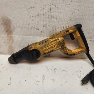 May include: A yellow and black DeWalt rotary hammer drill with a black power cord. The drill has visible wear and tear, with markings and numbers written on the body. The drill is designed for heavy-duty construction and demolition tasks.