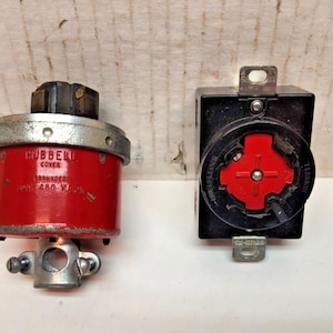 May include: Two electrical components: a red and silver Hubbell cover with text and a black electrical outlet with a red center. The Hubbell cover is cylindrical and the outlet is rectangular.