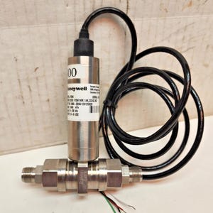 May include: A silver-colored Honeywell pressure transmitter with a black cable and a stainless steel fitting. The device has a label with text and is designed for industrial applications. The fitting has threaded ends and exposed wires.
