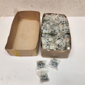 May include: Two cardboard boxes filled with small silver metal hardware. The boxes are sitting on a white surface. There are also several small bags of the same hardware on the surface.
