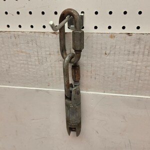 May include: A weathered metal swivel hook and connector, designed for heavy-duty use. The hook is attached to a pegboard, showcasing its industrial design. The metal has a worn, aged appearance, suggesting durability and resilience.
