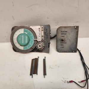 May include: A Cyclemaster control unit featuring a circular green and white dial, a metal gear, and a separate rectangular control plate with a toggle switch labeled Exercise Without Load and Exercise With Load, accompanied by four metal rods.