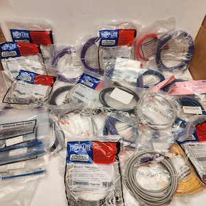 May include: A collection of various network cables, including Ethernet patch cables, in a cardboard box. Cables are in various colors, including blue, red, yellow, and gray, and are packaged in clear plastic bags with labels.