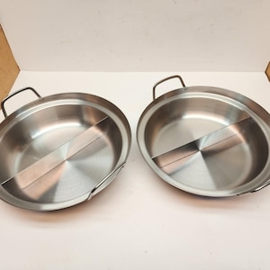 May include: Two stainless steel hot pot pans with a divider, each with a handle on either side. The pans are round with a brushed metal finish. The divider creates two separate cooking areas within each pan.