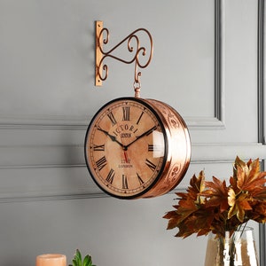 May include: A copper-toned clock with Roman numerals and a vintage design. The clock face reads "Victoria Station 1777 London". The clock is hanging from a copper-toned bracket.