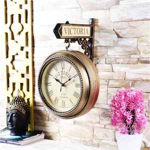 May include: A gold-toned double-sided clock with Roman numerals and a black sign that reads "VICTORIA STATION 1747 LONDON".