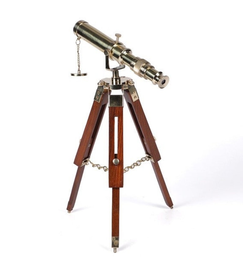 Pu&ograve; includere: Un telescopio in ottone con un treppiede in legno. Il telescopio &egrave; dorato e ha una catena attaccata ad esso. Il treppiede &egrave; in legno marrone scuro.
