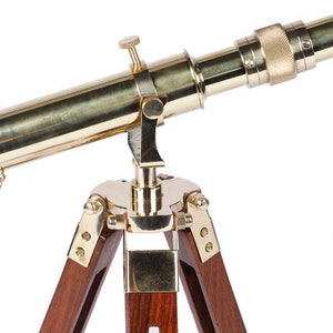 Pu&ograve; includere: Un telescopio in ottone con un treppiede in legno. Il telescopio &egrave; dorato e ha una manopola in ottone sul lato. Il treppiede &egrave; in legno scuro e ha tre gambe.