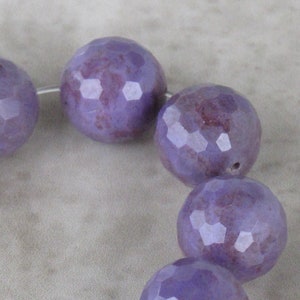 May include: A strand of purple faceted gemstone beads. The beads are round and have a slightly irregular shape. The beads are strung on a silver wire.