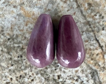 May include: Two purple ceramic teardrop-shaped beads with a glossy finish.