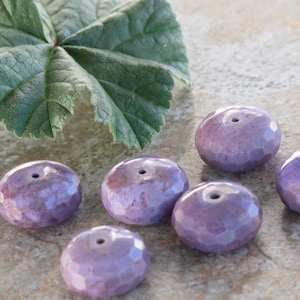 May include: Six purple ceramic beads with a hole in the center. The beads are faceted and have a glossy finish.
