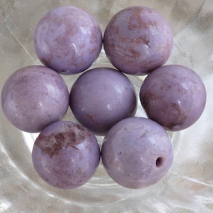 May include: Seven purple and brown marbled round beads in a bowl. The beads are smooth and have a natural, polished look.