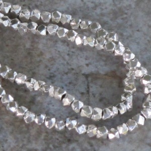 May include: A strand of silver-toned faceted beads. The beads are small and have a rough, irregular texture.