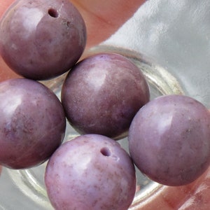 May include: Five round, purple beads with a hole drilled through the center. The beads are smooth and have a slight sheen.
