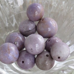 May include: A group of ten round, purple and white, polished, gemstone beads. The beads have a smooth, glossy finish and are arranged in a pyramid shape.