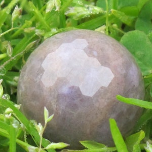 May include: A smooth, round, gray and white stone with a geometric pattern. The stone is sitting in a bed of green grass.