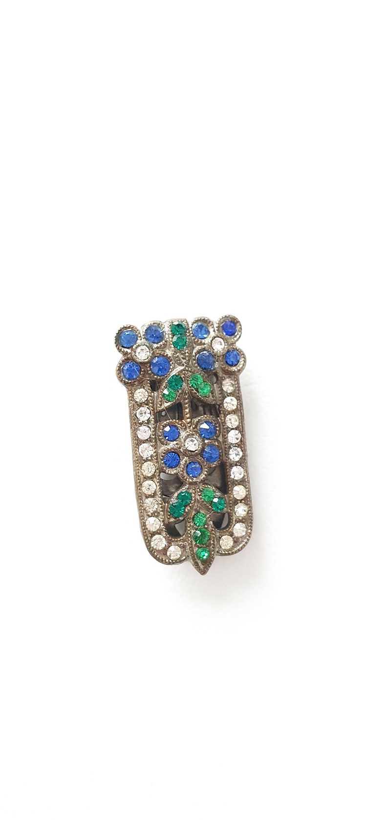 a 3 x 1 centimetre dress clip with rhinestones with two blue flowers with clear centres at the top, green leaves, a flower in the middle and more green leaves at the bottom, with a clear border of rhinestones down either side.