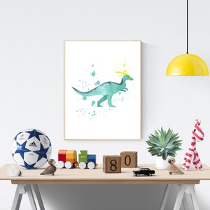 May include: A watercolor print of a green dinosaur with a yellow crown, surrounded by blue and green paint splatters. The print is framed and hanging on a white wall.