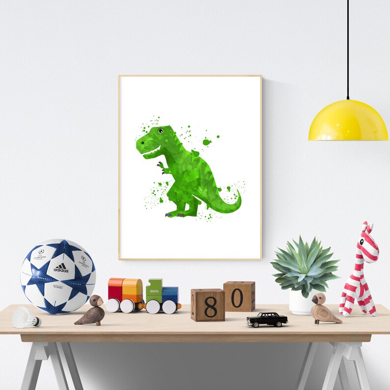 May include: A green watercolor dinosaur print with white splatters on a white background. The print is framed and hanging on a white wall above a wooden table with a soccer ball, wooden blocks, a toy train, and a potted plant.