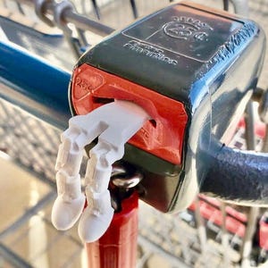 May include: A shopping cart coin release mechanism with a white, articulated hand-shaped token inserted. The mechanism is black and red, with the text "25¢" visible. The cart's handle is blue and silver.
