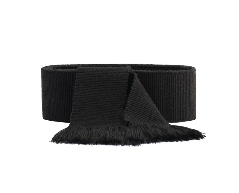May include: A black fabric scarf with a fringed edge. The scarf is folded in half and tied in a knot.
