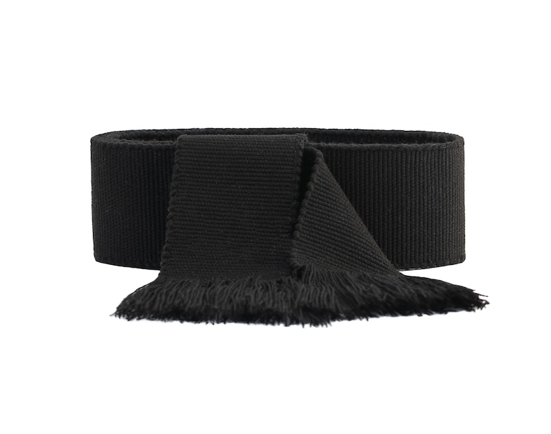 May include: A black fabric scarf with a fringed edge. The scarf is folded in half and tied in a knot.
