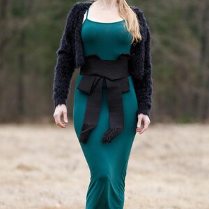 May include: A teal maxi dress with a black woven belt tied in a bow at the waist. The belt has fringe details.