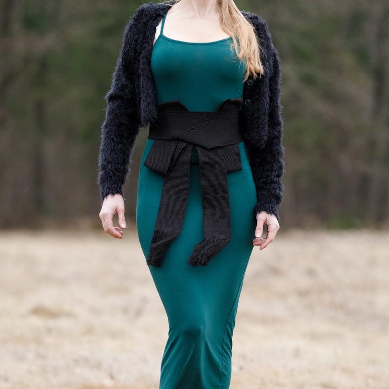 May include: A teal maxi dress with a black woven belt tied in a bow at the waist. The belt has fringe details.