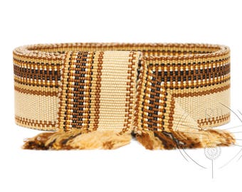 May include: A woven belt with a brown, white, and gold geometric pattern. The belt has a fringe on both ends.
