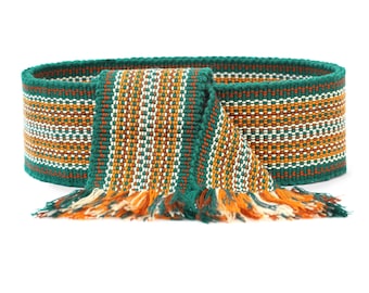 May include: A green, orange, and white woven belt with fringe tassels. The belt is made of a thick, textured fabric and has a geometric pattern.