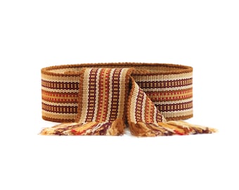 May include: A brown, orange, and white woven belt with fringe tassels. The belt is made of a thick, textured fabric and has a geometric pattern.