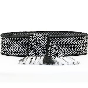 May include: Black and white woven belt with a fringe on the end. The belt has a chevron pattern.