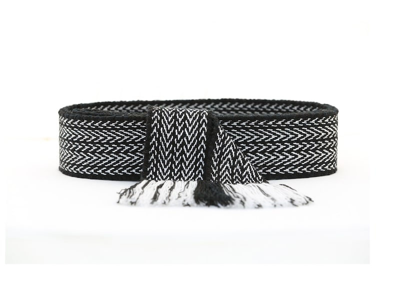 May include: Black and white woven belt with a fringe on the end. The belt has a chevron pattern.