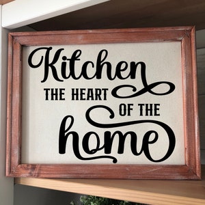 May include: A rustic wooden framed canvas sign with the text "Kitchen the heart of the home" in black cursive font.