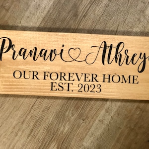 May include: A wooden sign with the text "Pranavi & Athreya Our Forever Home Est. 2023" in black lettering.